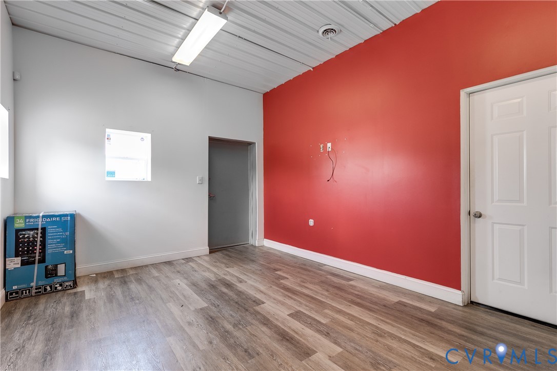 Interior room featuring wood-finish flooring, a ribbed metal ceiling, and linear fluorescent lighting Interior room featuring wood-finish flooring, a ribbed metal ceiling, and linear fluorescent lighting