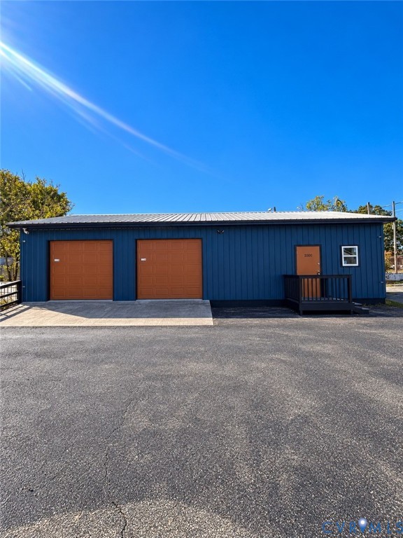 Detached metal-sided structure featuring two garage bays, a paved apron, and an elevated entry platform with railing
