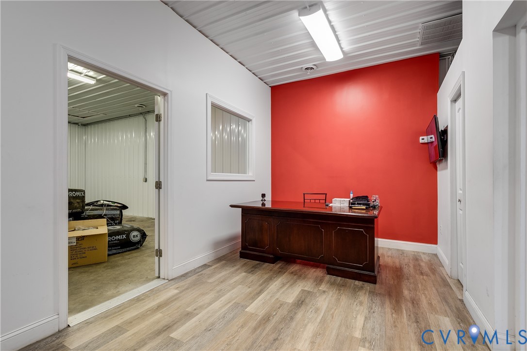 Interior space featuring wood-finish flooring, a metal corrugated ceiling, a fixed wall window, and integrated linear lighting Interior space featuring wood-finish flooring, a metal corrugated ceiling, a fixed wall window, and integrated linear lighting