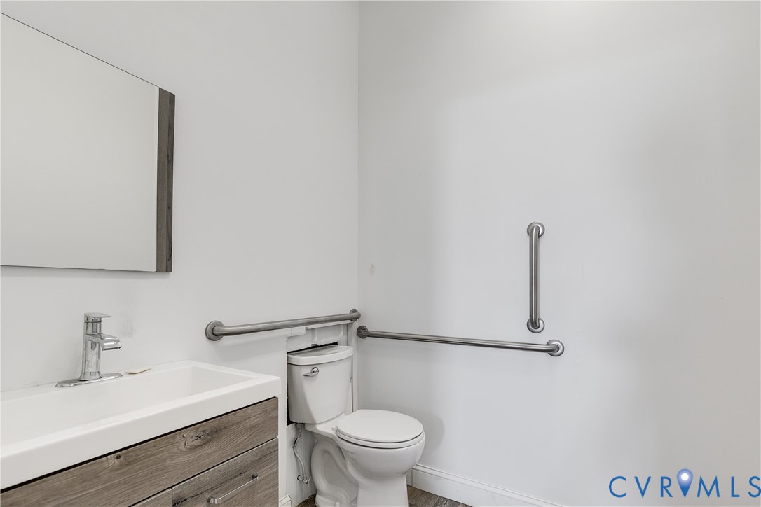 Wall-mounted vanity with a rectangular sink, wood-finish cabinetry, frameless mirror, and integrated brushed metal safety grab bars Wall-mounted vanity with a rectangular sink, wood-finish cabinetry, frameless mirror, and integrated brushed metal safety grab bars