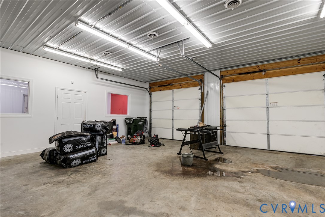 Multi-car garage featuring dual overhead doors, concrete flooring, high-clearance metal panel ceiling, and integrated fluorescent lighting Multi-car garage featuring dual overhead doors, concrete flooring, high-clearance metal panel ceiling, and integrated fluorescent lighting