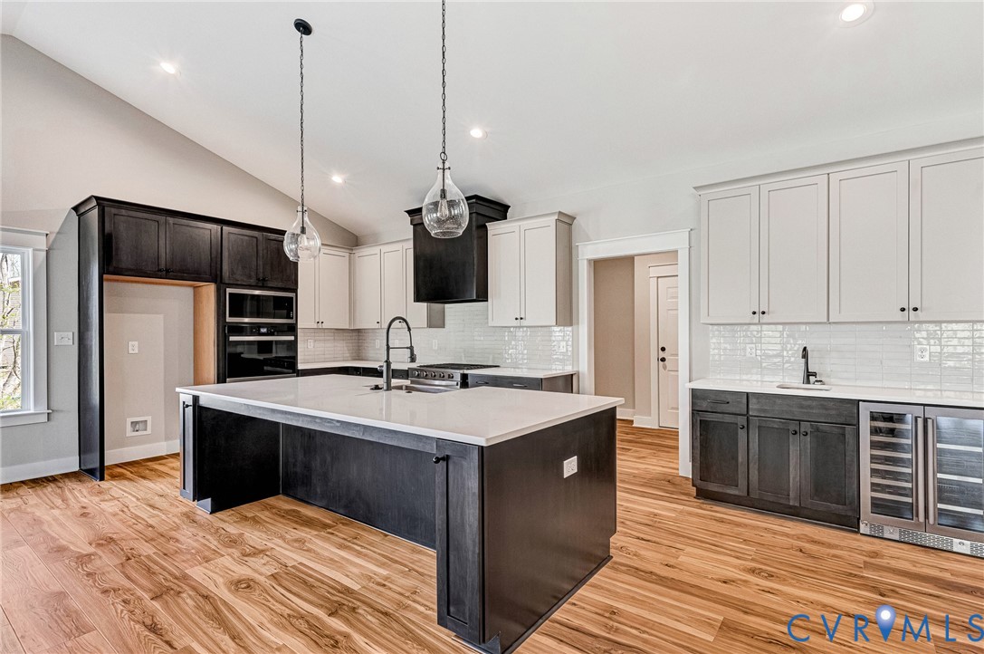 Open concept kitchen featuring hardwood floors, a spacious central island with a sink, white countertops, and both light and dark cabinetry