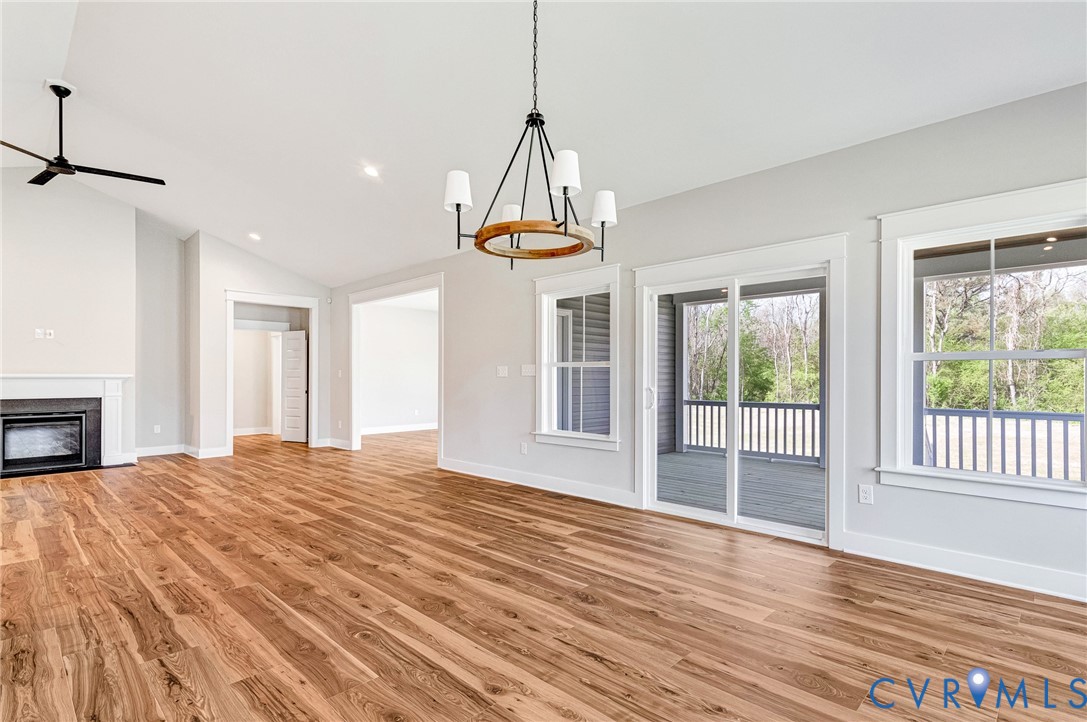 Spacious living area featuring hardwood floors, a fireplace with a white mantle, an exposed beam chandelier, and access to an outdoor deck