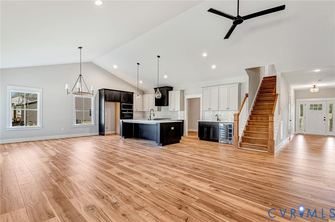 Expansive open-concept living area featuring light wood flooring, a kitchen with an island, and a prominent staircase