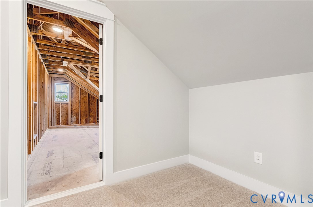 A partially finished attic space featuring a window and exposed wooden beams, offering potential for further development