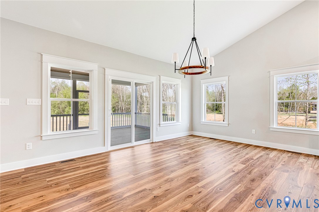 Spacious room featuring vaulted ceilings, a contemporary chandelier, and hardwood floors