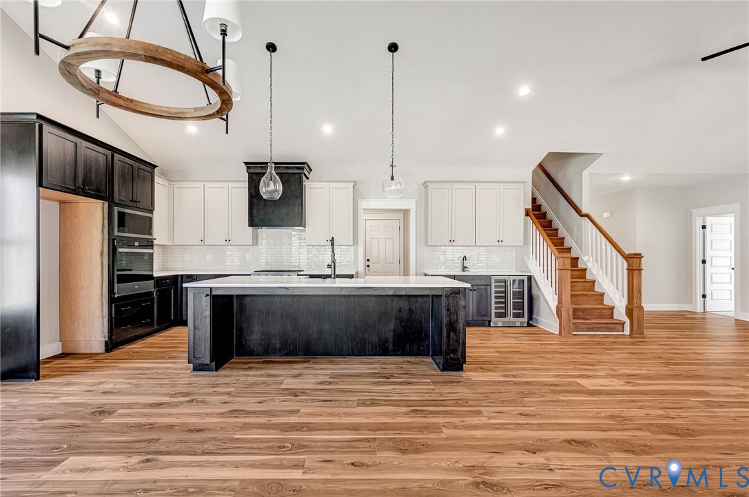 Expansive open-concept living area featuring wood flooring, a kitchen with an island, and a staircase with natural wood treads and railing