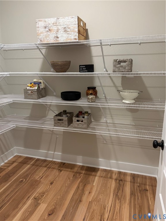 Spacious storage area featuring L-shaped wire shelving, wood-finish flooring, white baseboards, and a paneled door with a black knob