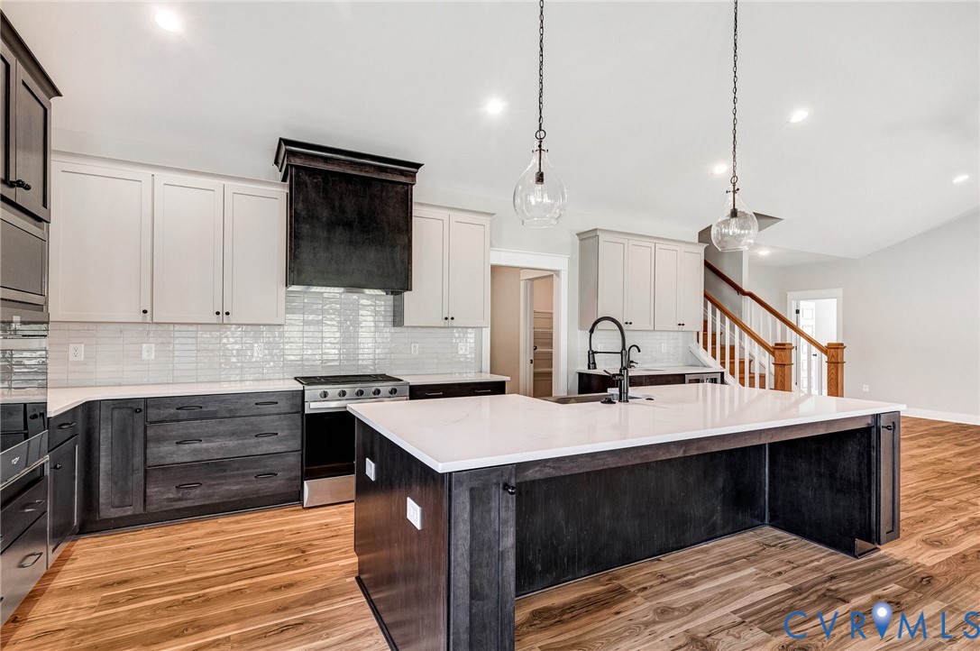 The kitchen features a large island with a white countertop, two-tone cabinetry, a stainless steel range, and a white subway tile backsplash
