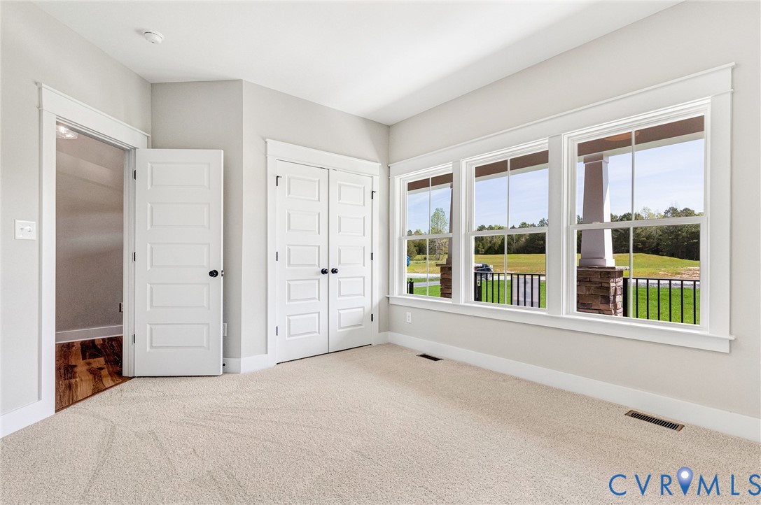 This inviting room features light-colored carpeting, three large windows offering views of green landscaping, and white paneled doors with black hardware