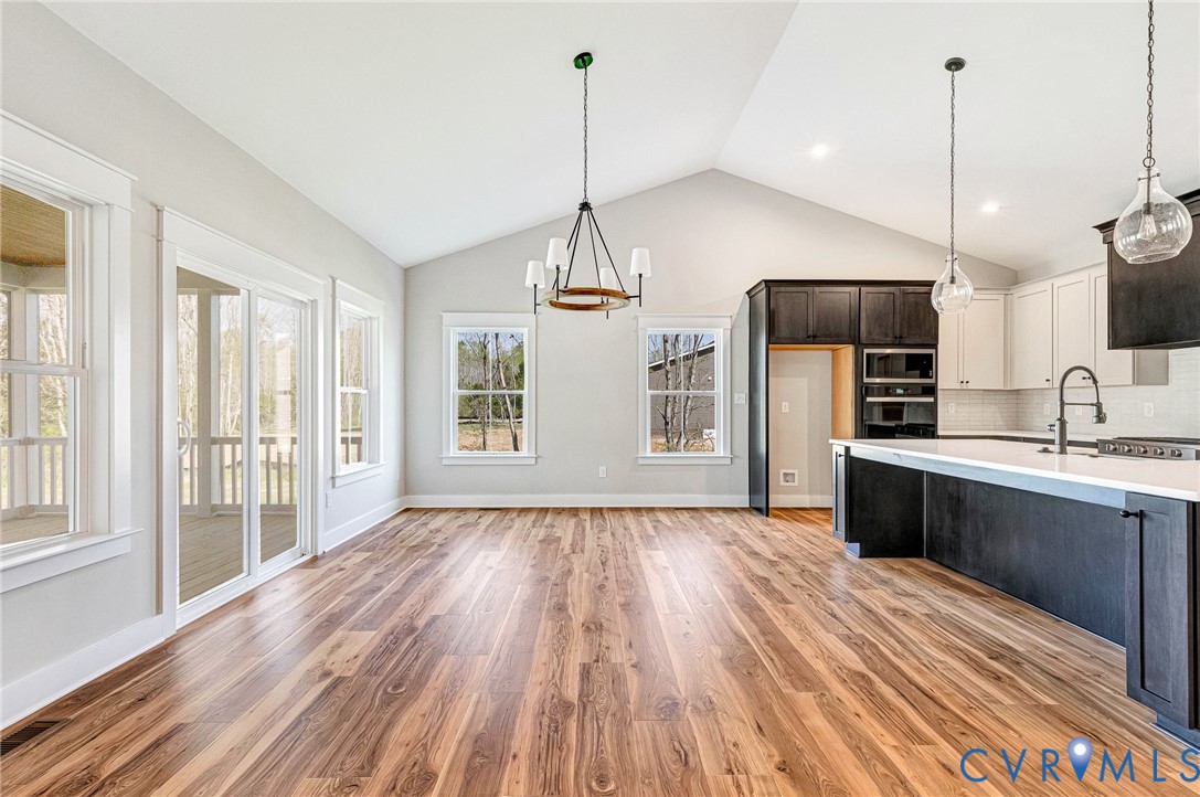 Spacious open concept living area featuring vaulted ceilings, rich hardwood flooring, a modern kitchen with a large island and pendant lighting, and access to an outdoor screened porch