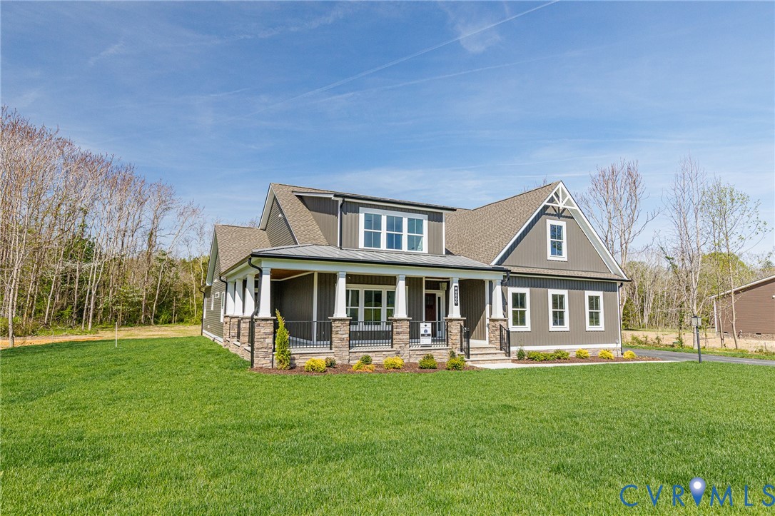 The property features a charming front porch with white columns and stone accents, a well-maintained green lawn, and a light brown roof