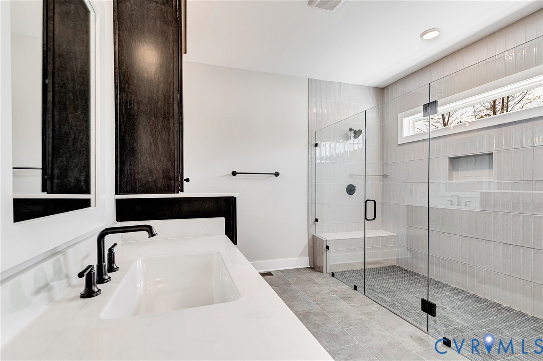 The bathroom features a sleek vanity with a rectangular sink and matte black fixtures, a spacious walk-in shower with glass doors, a built-in shower bench, and a horizontal window