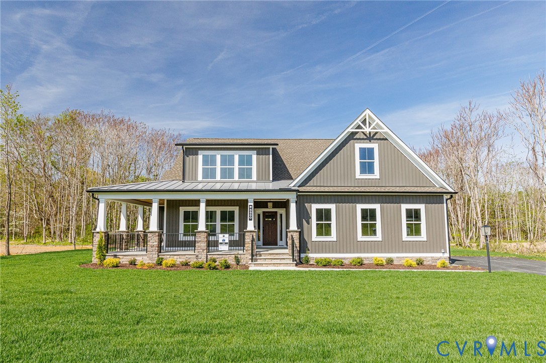 The property features a charming exterior with grey siding, a covered porch with white pillars and stone accents, and an expansive front lawn