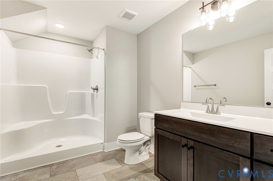 Bathroom featuring a white shower stall, a toilet, a vanity with a dark wood finish, a white countertop with an integrated sink, and a large mirror