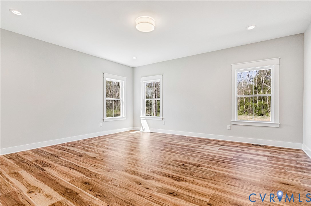 This bright room features wide plank wood flooring, light grey walls, white trim, and three windows that provide views of trees