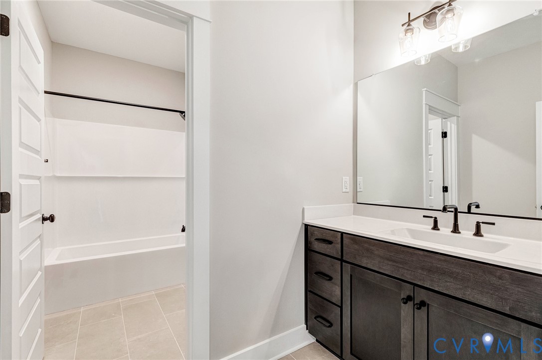 The bathroom features a vanity with a white countertop and a rectangular sink, complemented by a large mirror and modern light fixture
