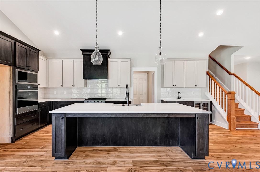 The kitchen features a large island with a white countertop and dark cabinetry, pendant lighting, and stainless steel appliances