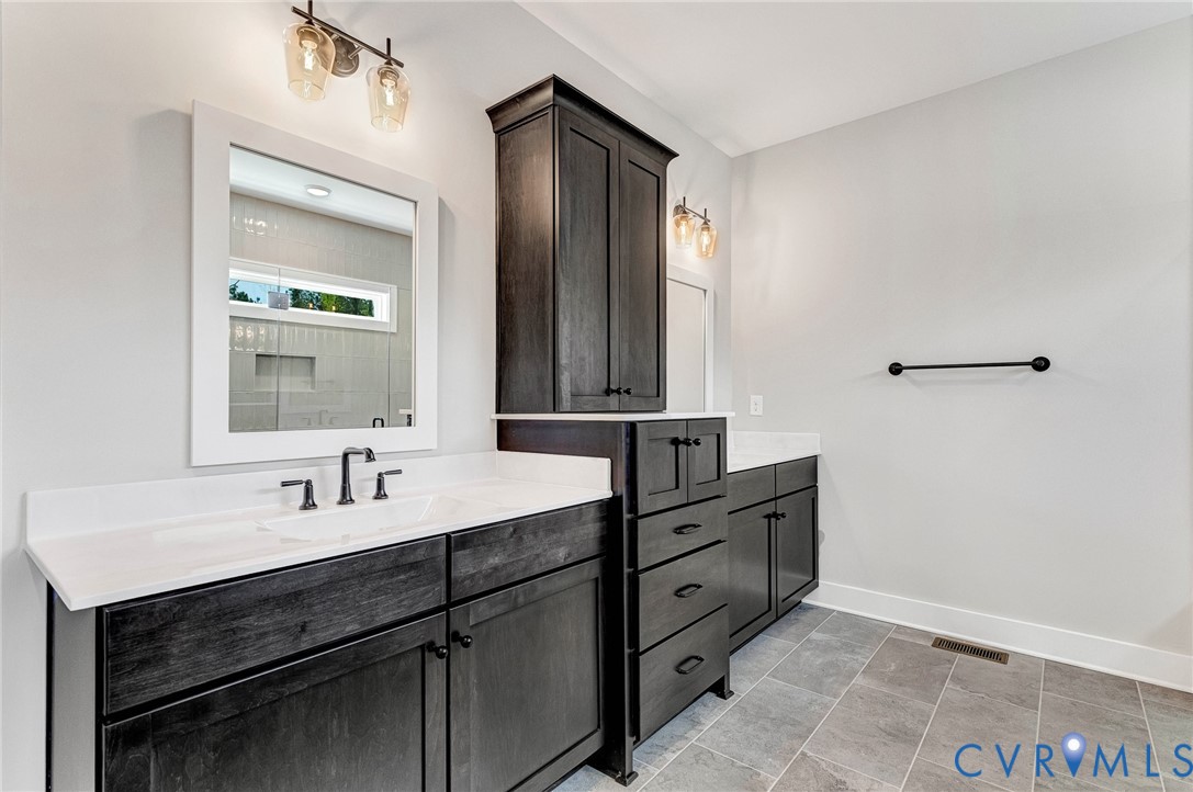 Bathroom featuring dual dark wood vanities with white countertops, a tall dark wood storage cabinet, and tiled flooring