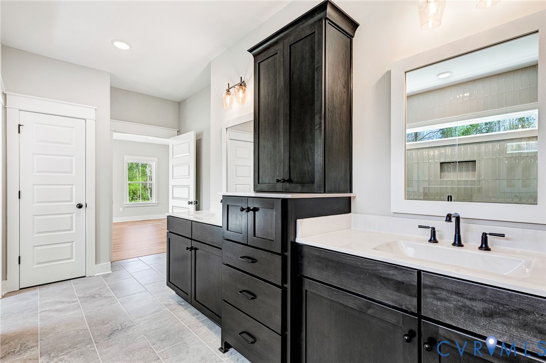 This bathroom features dual vanities with dark cabinetry and white countertops, a large framed mirror, and tiled flooring