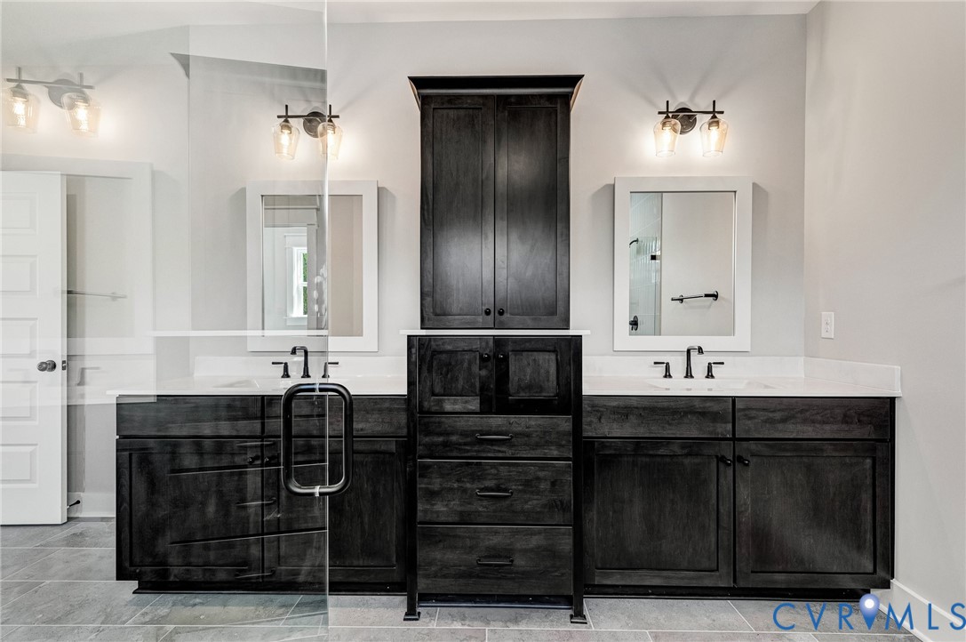 Well-appointed bathroom featuring dual vanities with dark wood cabinetry and white countertops, illuminated by wall-mounted light fixtures