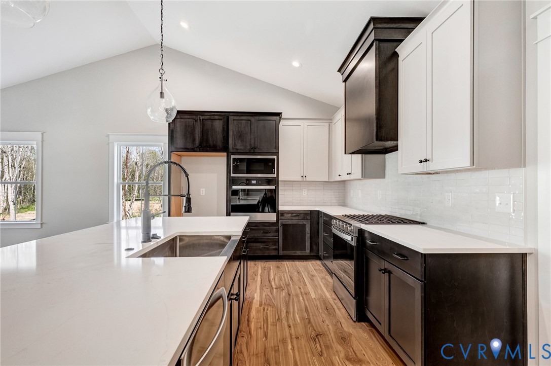 Kitchen featuring a vaulted ceiling, recessed lighting, white countertops, wood flooring, and a gas range