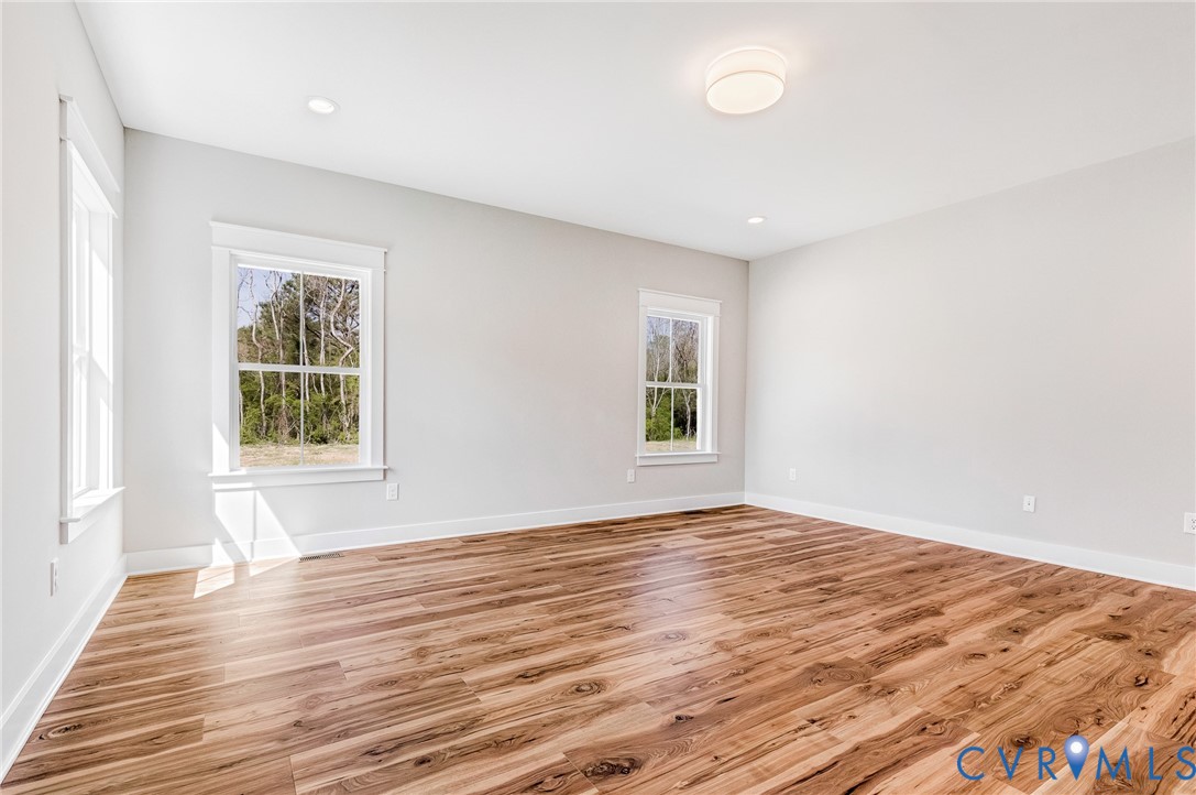 This spacious room features light-toned walls, rich wooden flooring, and multiple windows that provide views of outside greenery