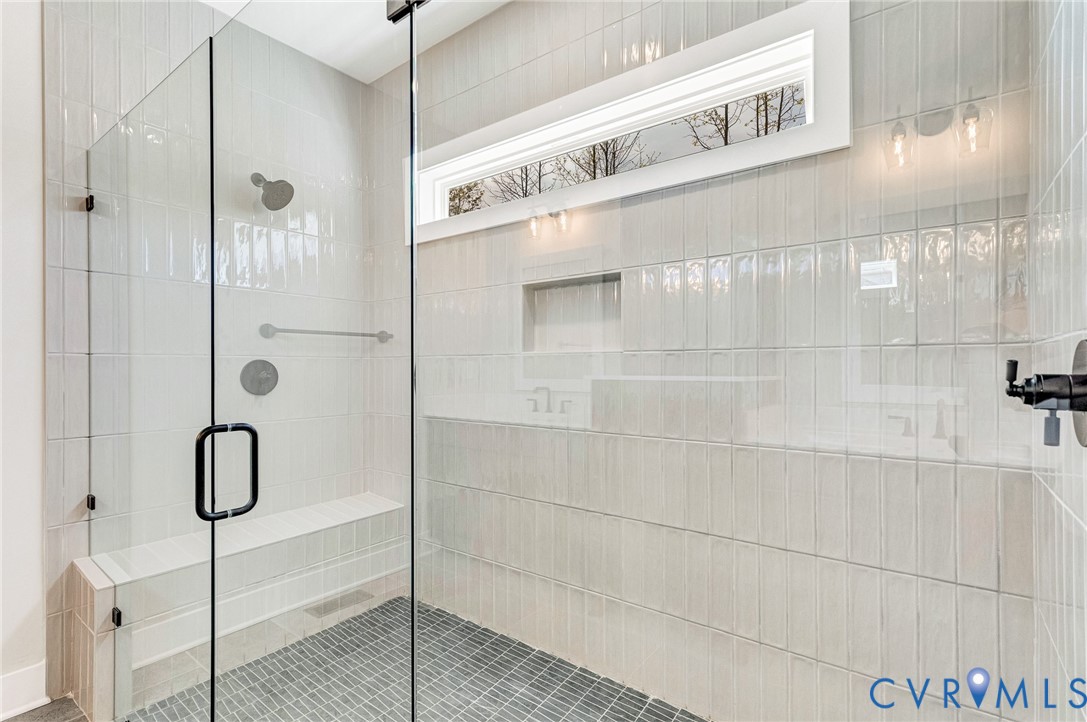 The shower features clear glass enclosure, light-colored rectangular wall tiles, and a built-in bench