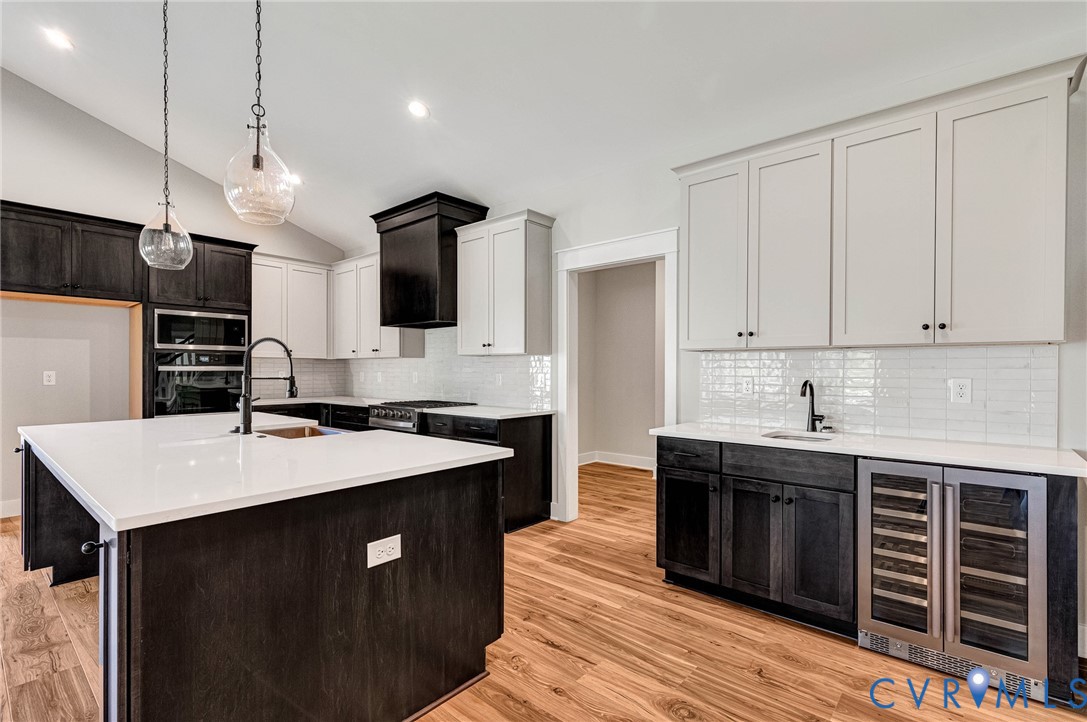 The kitchen features an expansive island with a white countertop and a sink with a matte black faucet, hardwood flooring, two-tone cabinetry, and a subway tile backsplash