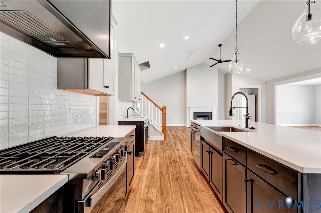 The kitchen features a large island with a stainless steel sink and a contemporary black faucet, a white tiled backsplash, and a stainless steel oven with a range hood