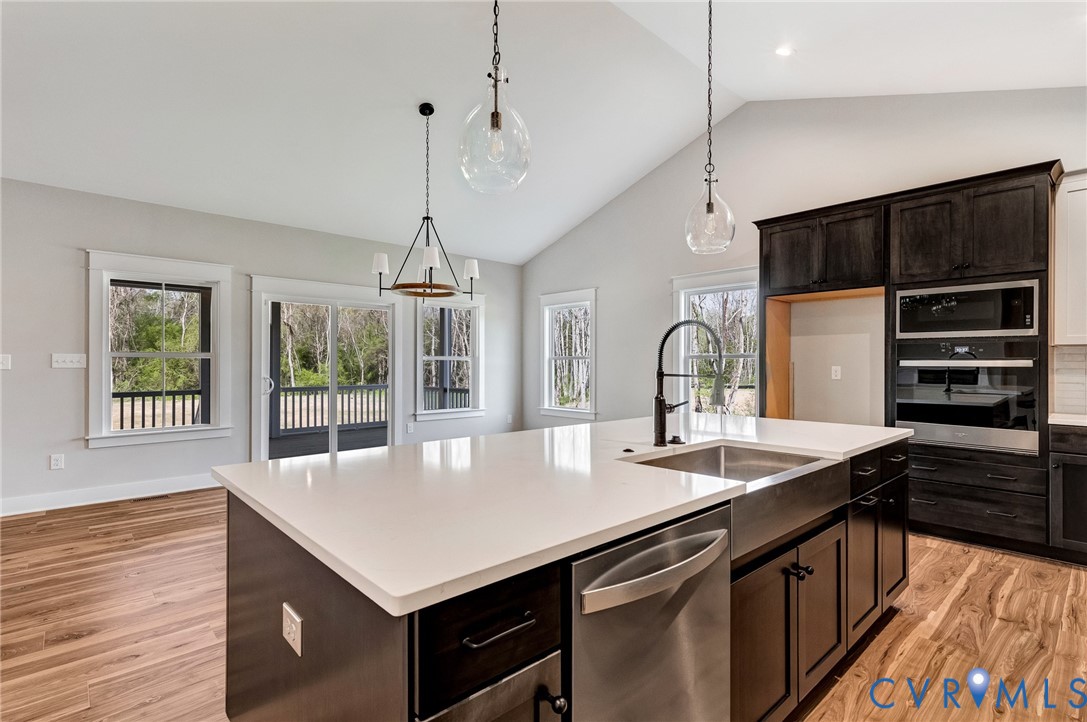 Kitchen featuring an island with a stainless steel sink and faucet, integrated dishwasher, and light-colored countertop
