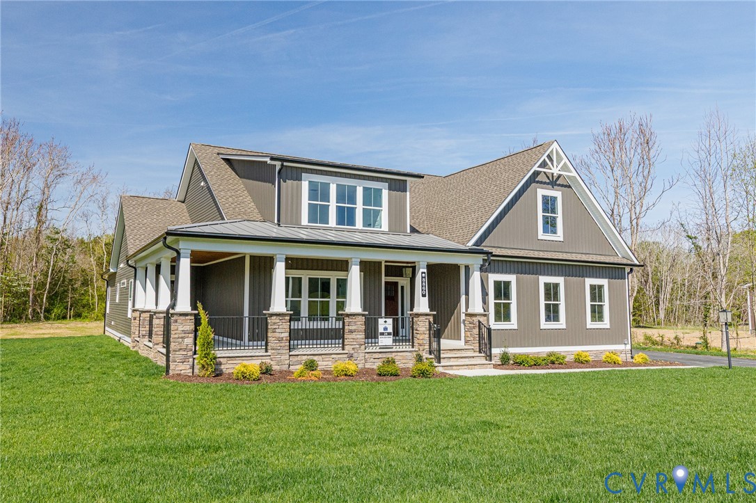 The property features a large front lawn, a covered porch with white columns and stone accents, and dark gray siding with white trim