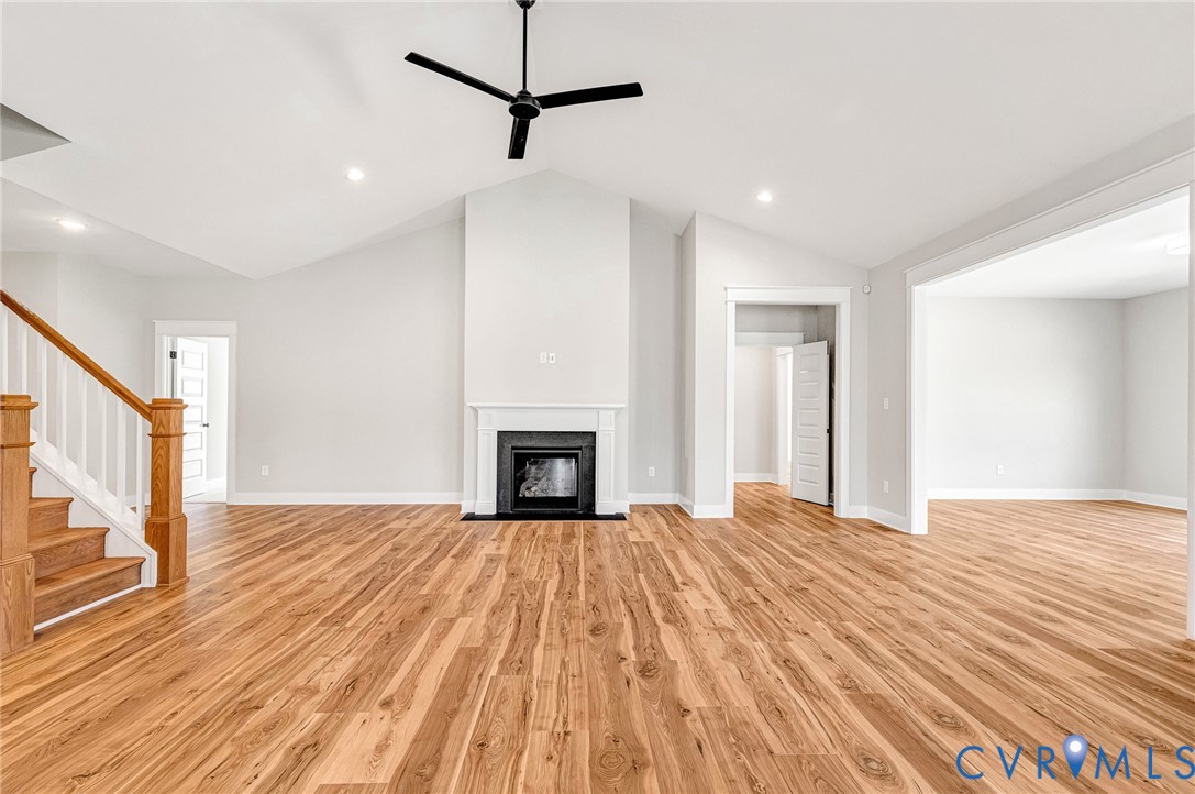 Spacious living area featuring hardwood flooring, a fireplace with a white mantel, and a ceiling fan
