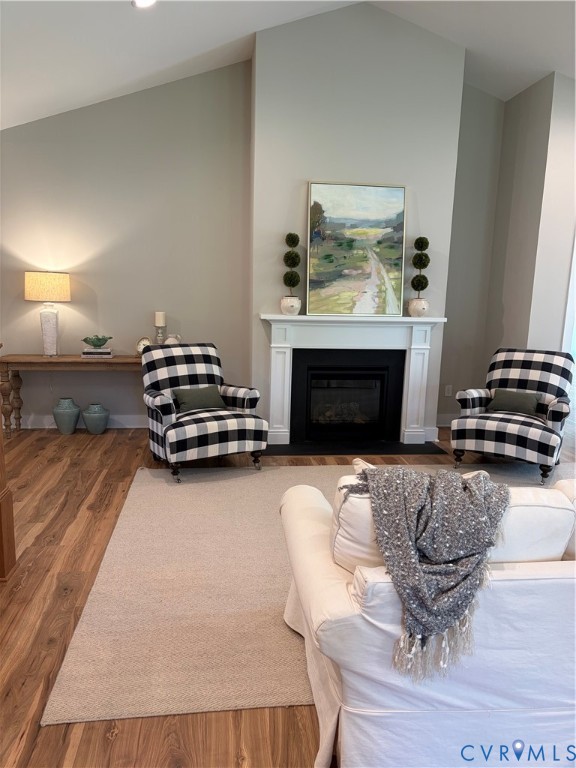 Living area featuring a vaulted ceiling, wood-finish flooring, a fireplace with a white mantel, and recessed lighting