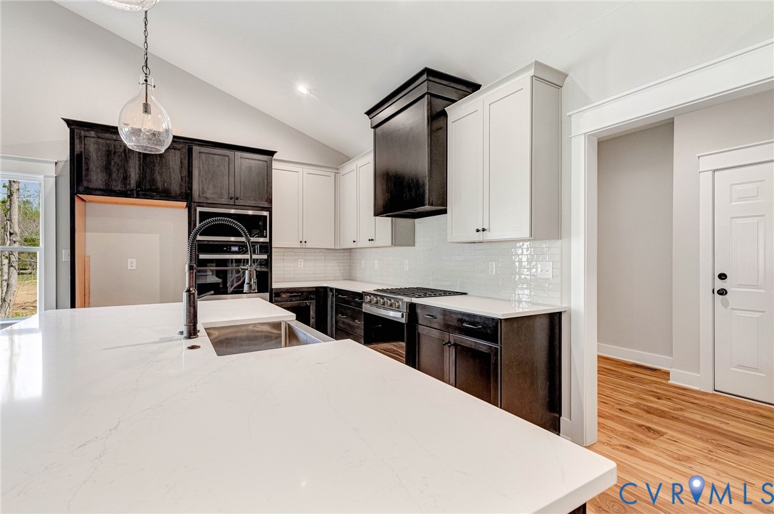 Modern kitchen with a spacious island featuring a sink and a contemporary faucet, white countertops, a gas range, and two-tone cabinetry with black and white finishes