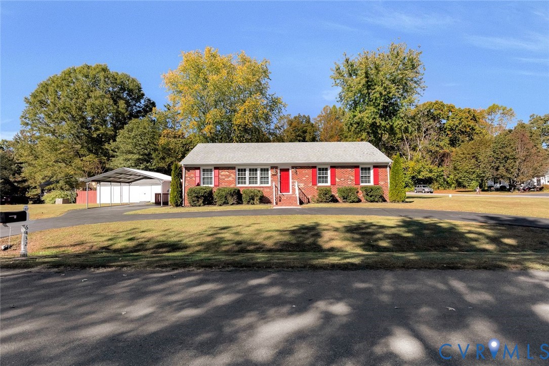 Single-story brick residence featuring a front-facing gable roof, vibrant red exterior shutters, an asphalt driveway, and a detached metal carport