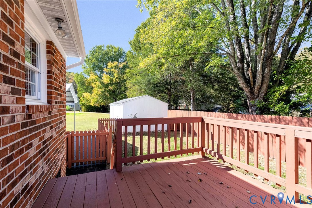Red brick exterior with a wooden deck, slatted wood perimeter fencing, and a detached metal storage structure Red brick exterior with a wooden deck, slatted wood perimeter fencing, and a detached metal storage structure