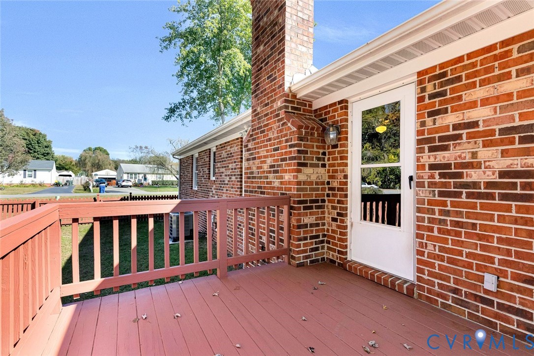 Exterior brick facade featuring a raised wooden deck with railings, an integrated brick chimney, and a glass-paneled entry door Exterior brick facade featuring a raised wooden deck with railings, an integrated brick chimney, and a glass-paneled entry door