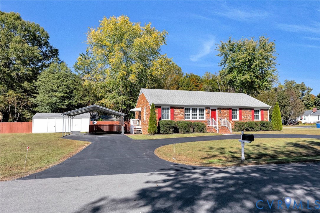 Brick exterior residence featuring red window shutters, a paved driveway, and an attached metal-frame carport