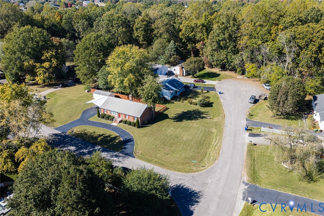 Brick exterior residence featuring a circular asphalt driveway, detached storage structure, and expansive grass lawn situated on a wooded lot Brick exterior residence featuring a circular asphalt driveway, detached storage structure, and expansive grass lawn situated on a wooded lot