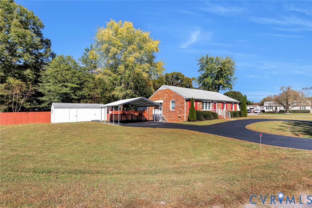 Brick exterior featuring a metal-roofed carport, asphalt driveway, detached storage structure, and fenced grounds