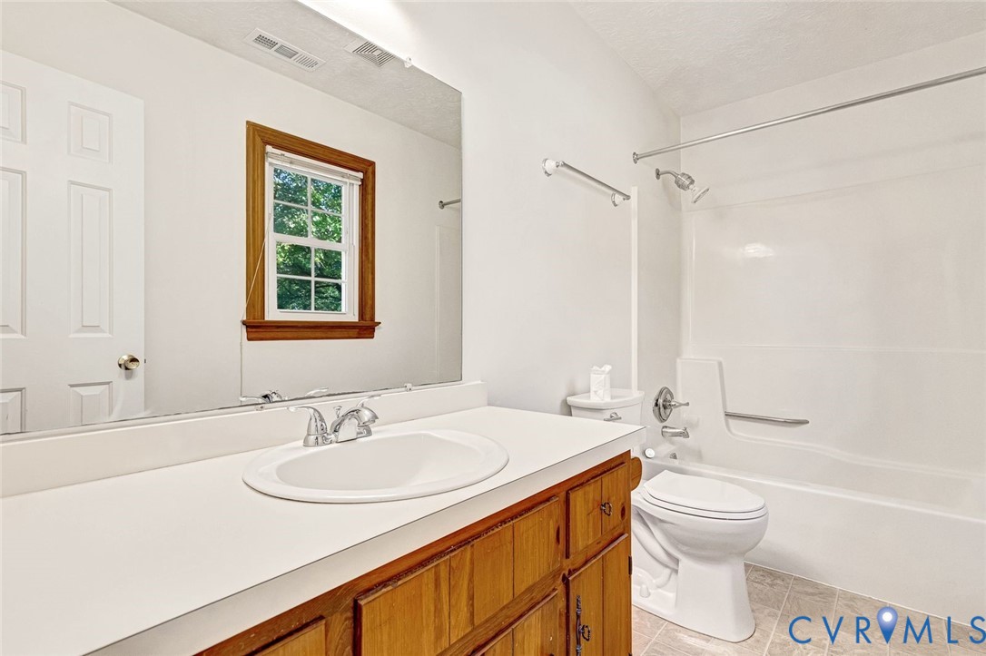 Bathroom featuring a wood-finish vanity with a white countertop and oval undermount sink, large wall-mounted mirror, combination tub and shower with a chrome fixture, and a window with wood trim