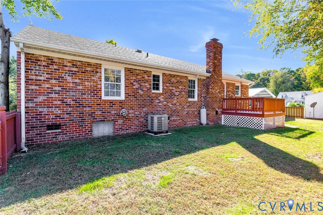 Exterior rear elevation featuring red brick siding, a raised wood deck with lattice skirting, and a masonry chimney Exterior rear elevation featuring red brick siding, a raised wood deck with lattice skirting, and a masonry chimney