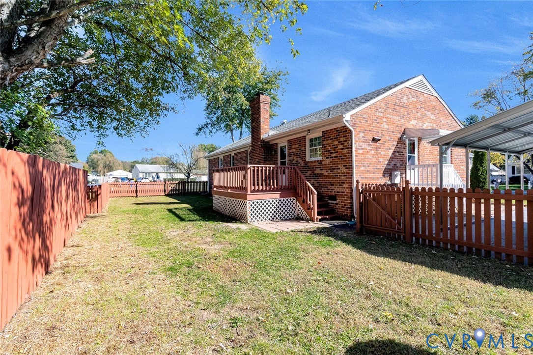 Brick exterior residence featuring a raised wood deck, lattice skirting, metal-covered carport, and enclosed yard with wood privacy fencing Brick exterior residence featuring a raised wood deck, lattice skirting, metal-covered carport, and enclosed yard with wood privacy fencing