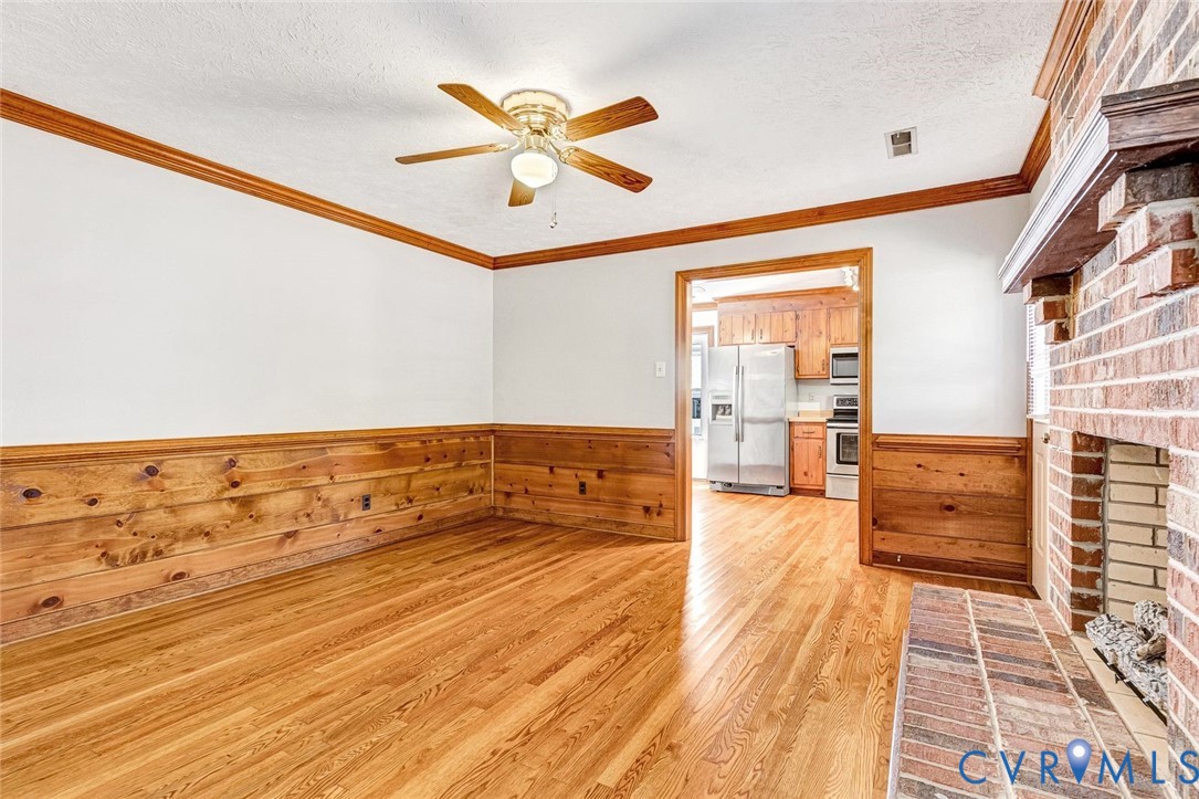 Living area featuring wood-finish flooring, wood wall paneling, crown molding, and a full-height brick fireplace