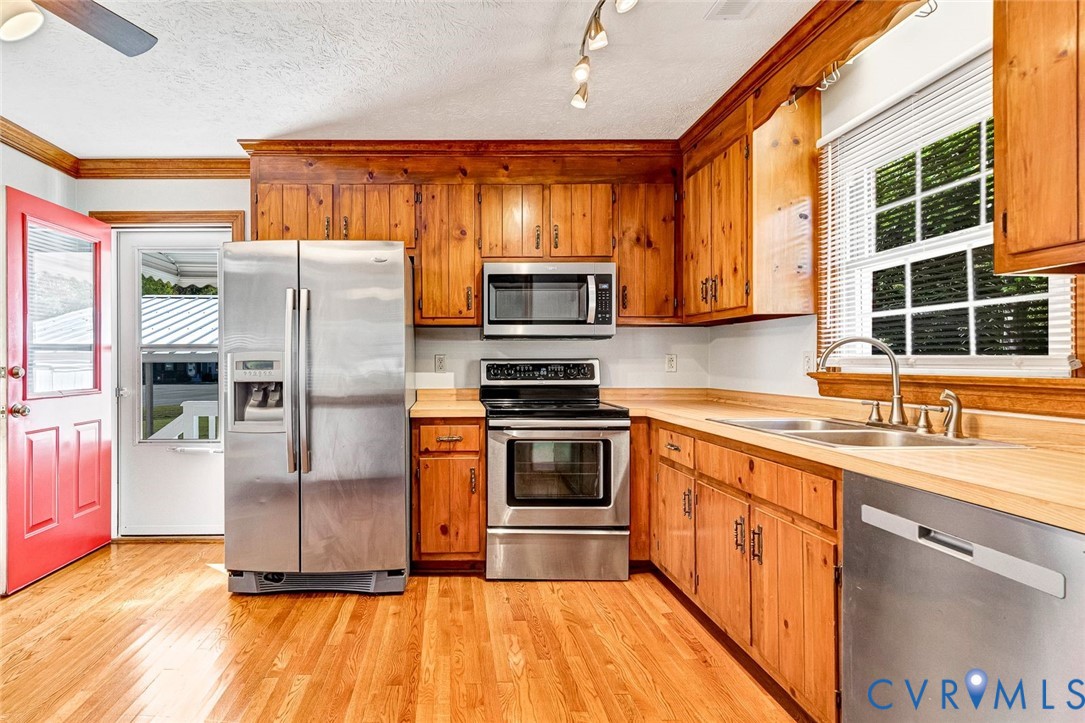 Kitchen featuring natural wood cabinetry, stainless steel appliances, wood-finish flooring, dual-basin sink, and recessed lighting