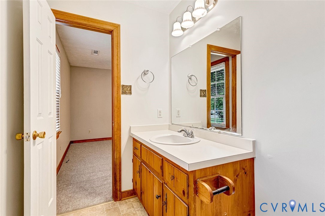 Vanity featuring wood cabinetry, a solid-surface countertop with an integrated basin, a large wall-mounted mirror, and a three-light fixture