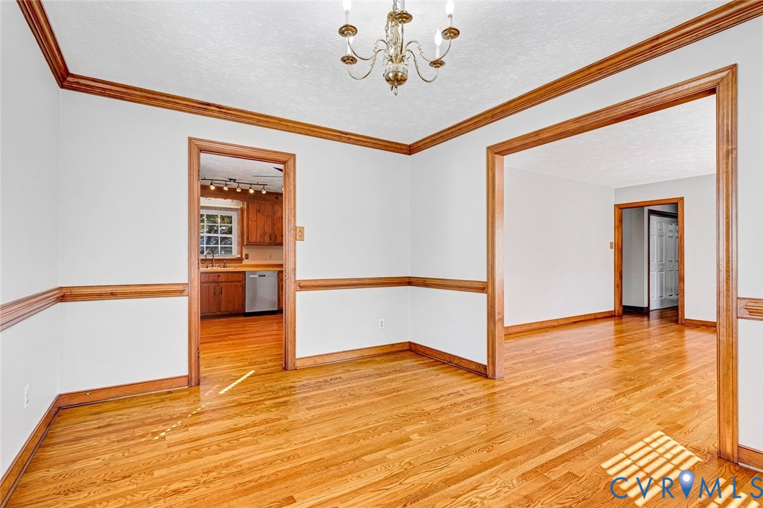 Interior space featuring wood-finish flooring, crown molding, chair rail trim, and a multi-arm chandelier