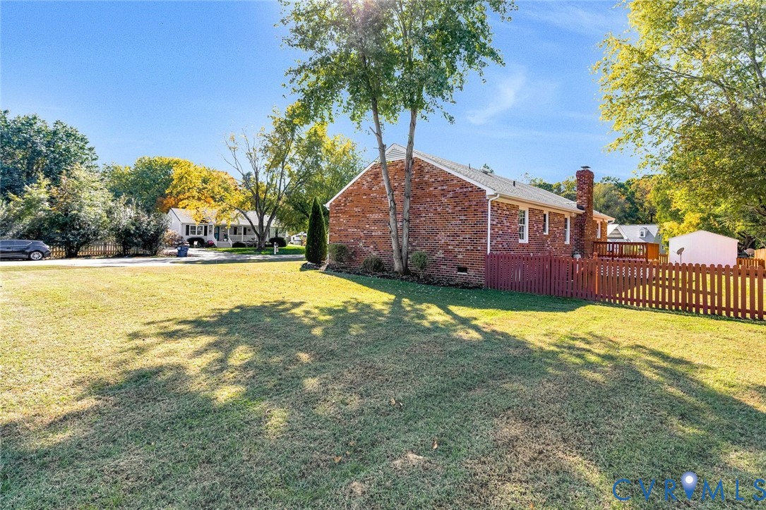 Brick exterior residence featuring an attached chimney, wood-style fencing, and a dedicated outdoor deck area situated on a large lot Brick exterior residence featuring an attached chimney, wood-style fencing, and a dedicated outdoor deck area situated on a large lot