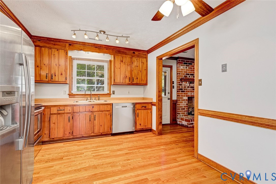 Kitchen featuring wood cabinetry, stainless steel appliances, wood-finish flooring, crown molding, and recessed track lighting